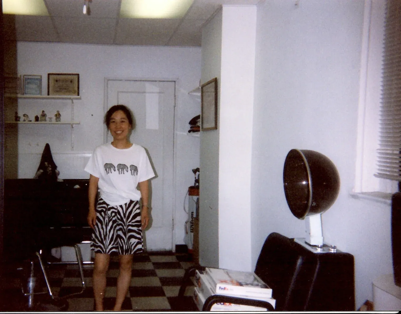 Anna smiling in her beauty salon, with a hood hair dryer and a salon chair beside her