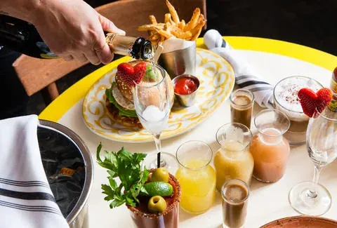 Champagne poured into a glass at the Black Ant beside a burger, Bloody Mary, and a flight of brunch drinks