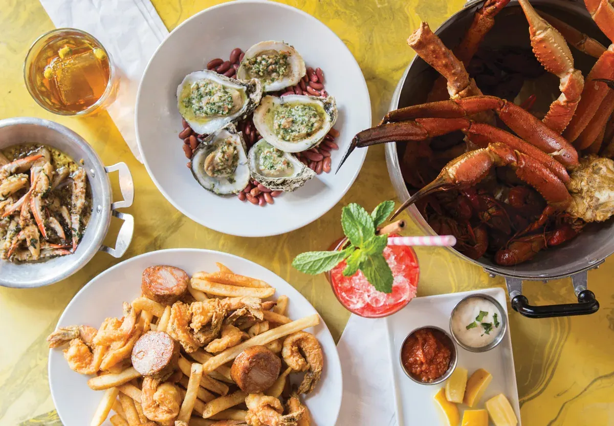 Overhead view of Bonton’s seafood brunch spread with grilled oysters, a crab leg pot, fried shrimp with fries, and cocktails