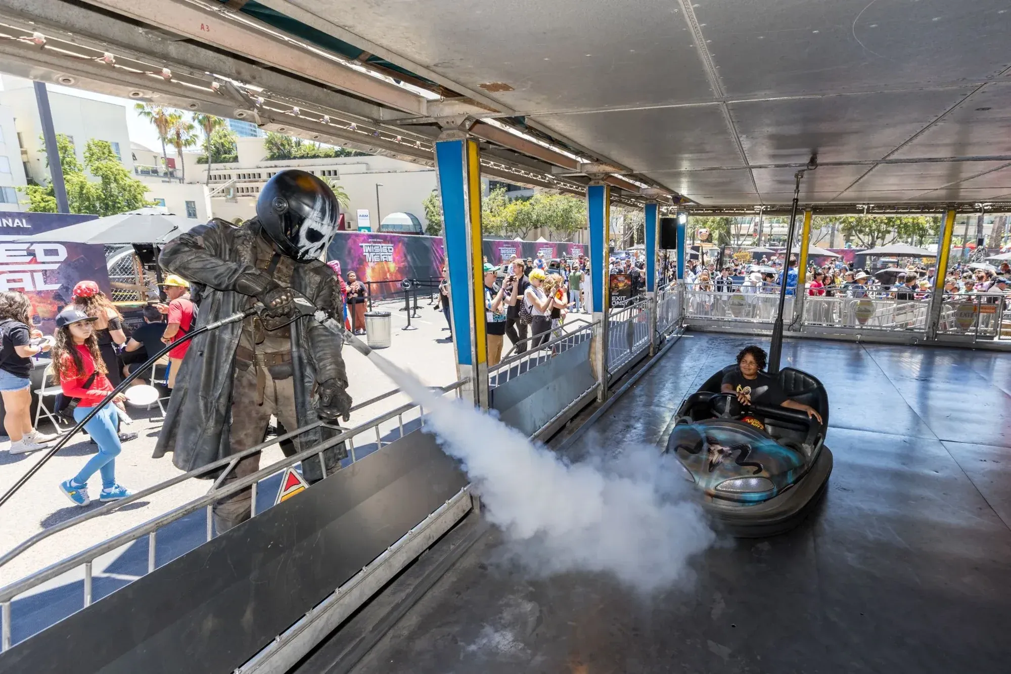 A Twisted Metal character blasts smoke beside a fan driving a bumper car in the Bumper Battle arena