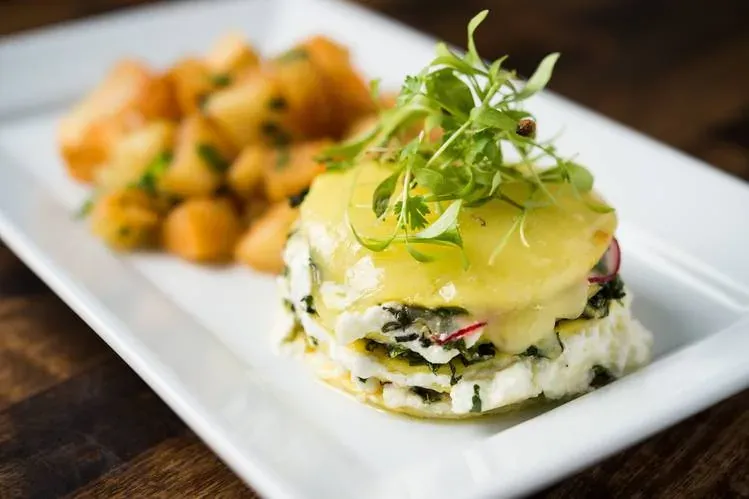 Dirt Candy vegetable brunch dish of a layered greens and cheese stack topped with microgreens, with roasted potatoes