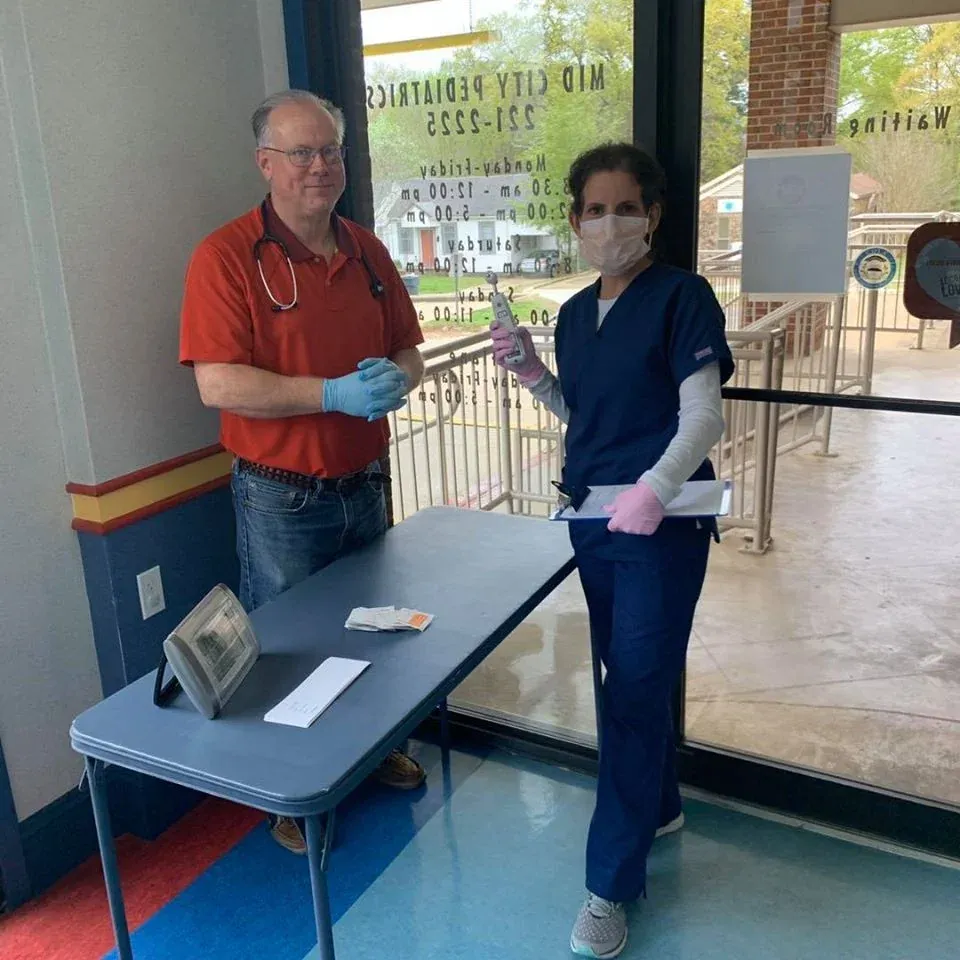 Mid City Pediatrics staff in gloves at a screening table by the clinic entrance