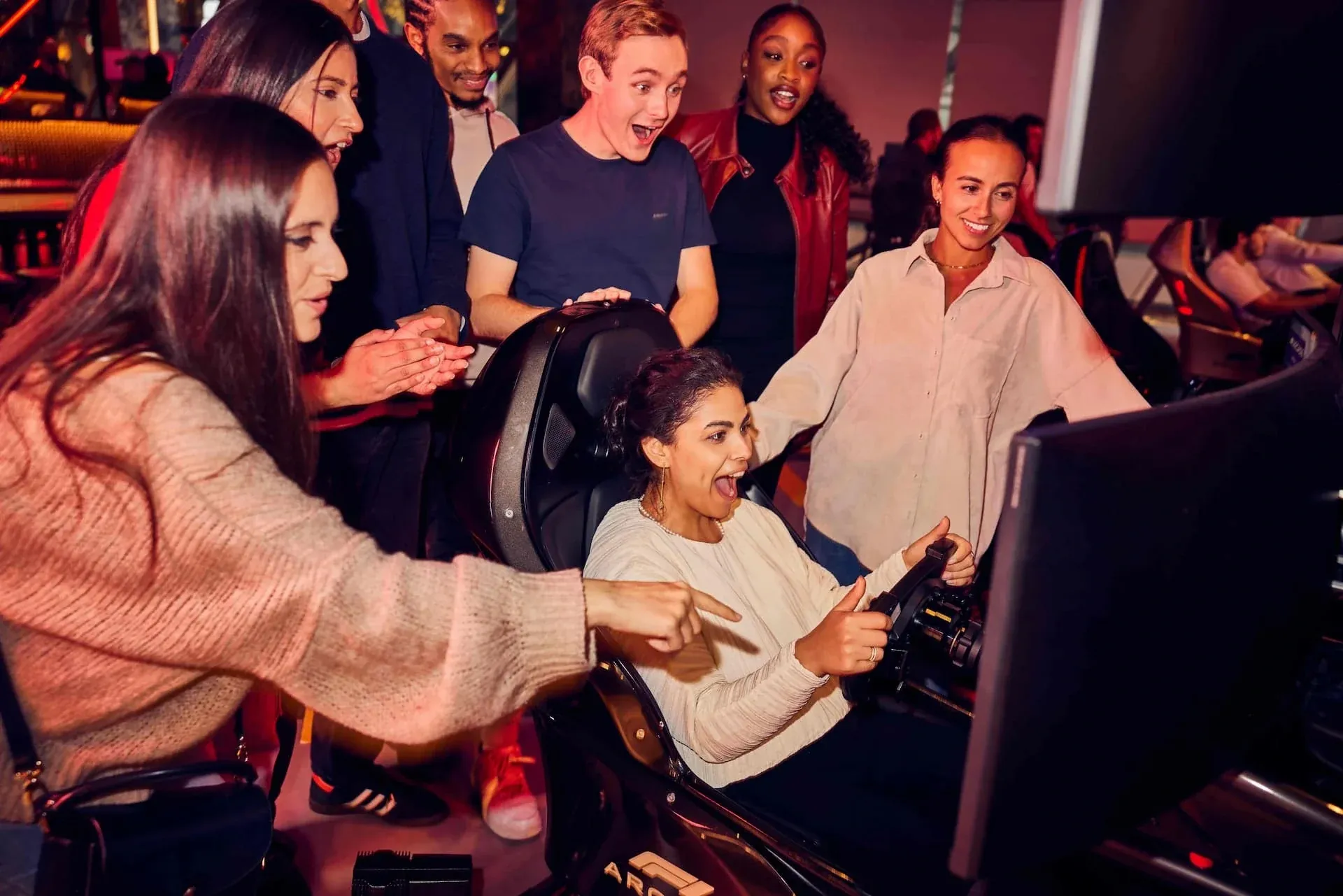 Friends cheering on a guest driving an F1 Arcade racing simulator