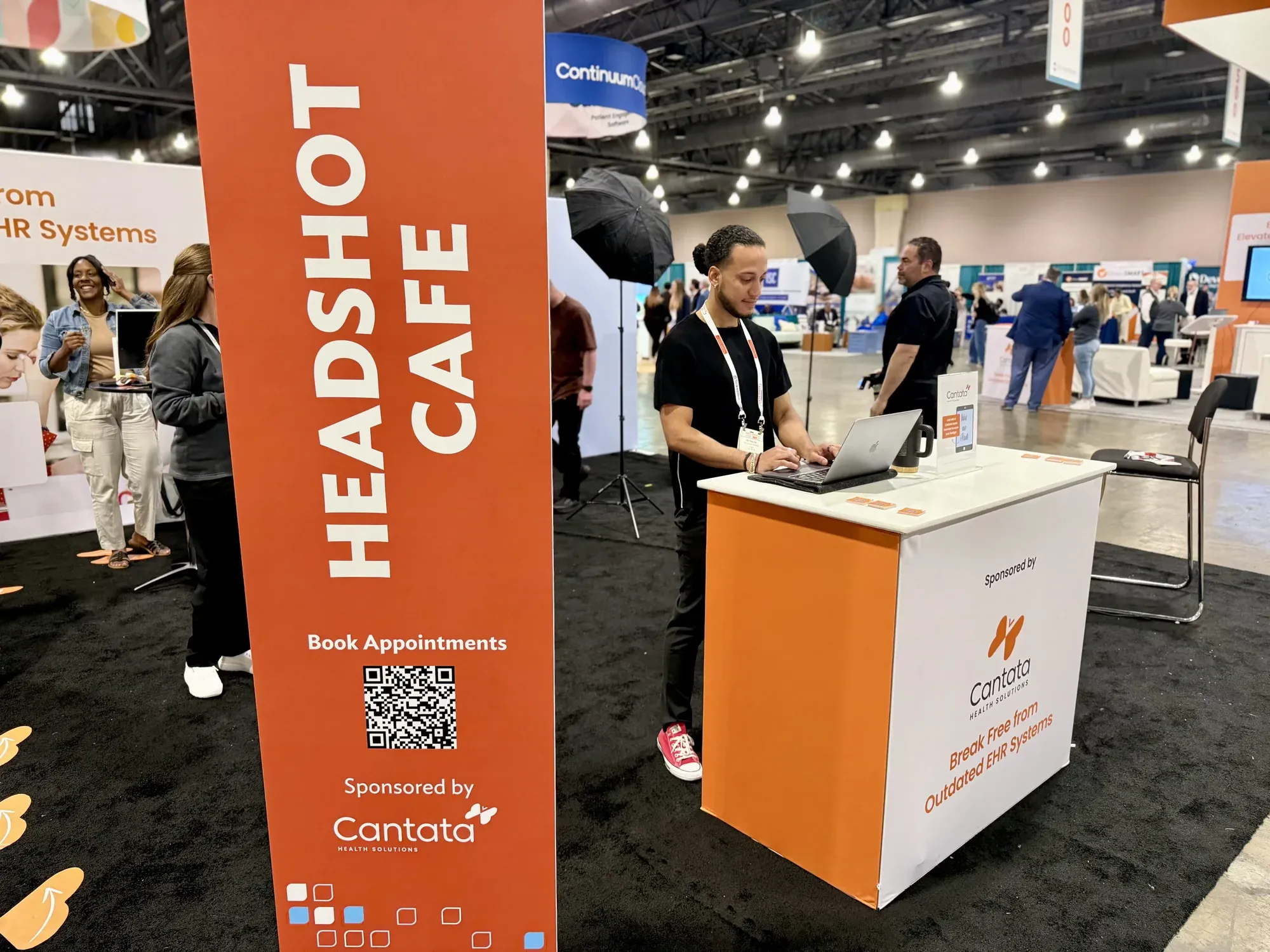An attendee checks in at the Headshot Café stand next to a QR code sign sponsored by Cantata