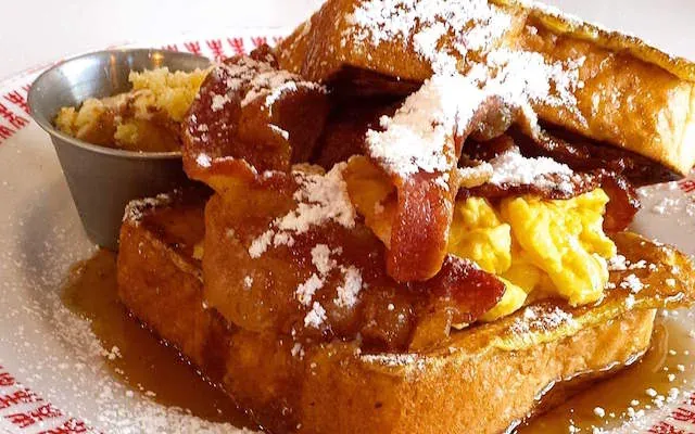 Le Petit Marché French toast sandwich stuffed with bacon and scrambled eggs, dusted with powdered sugar and syrup