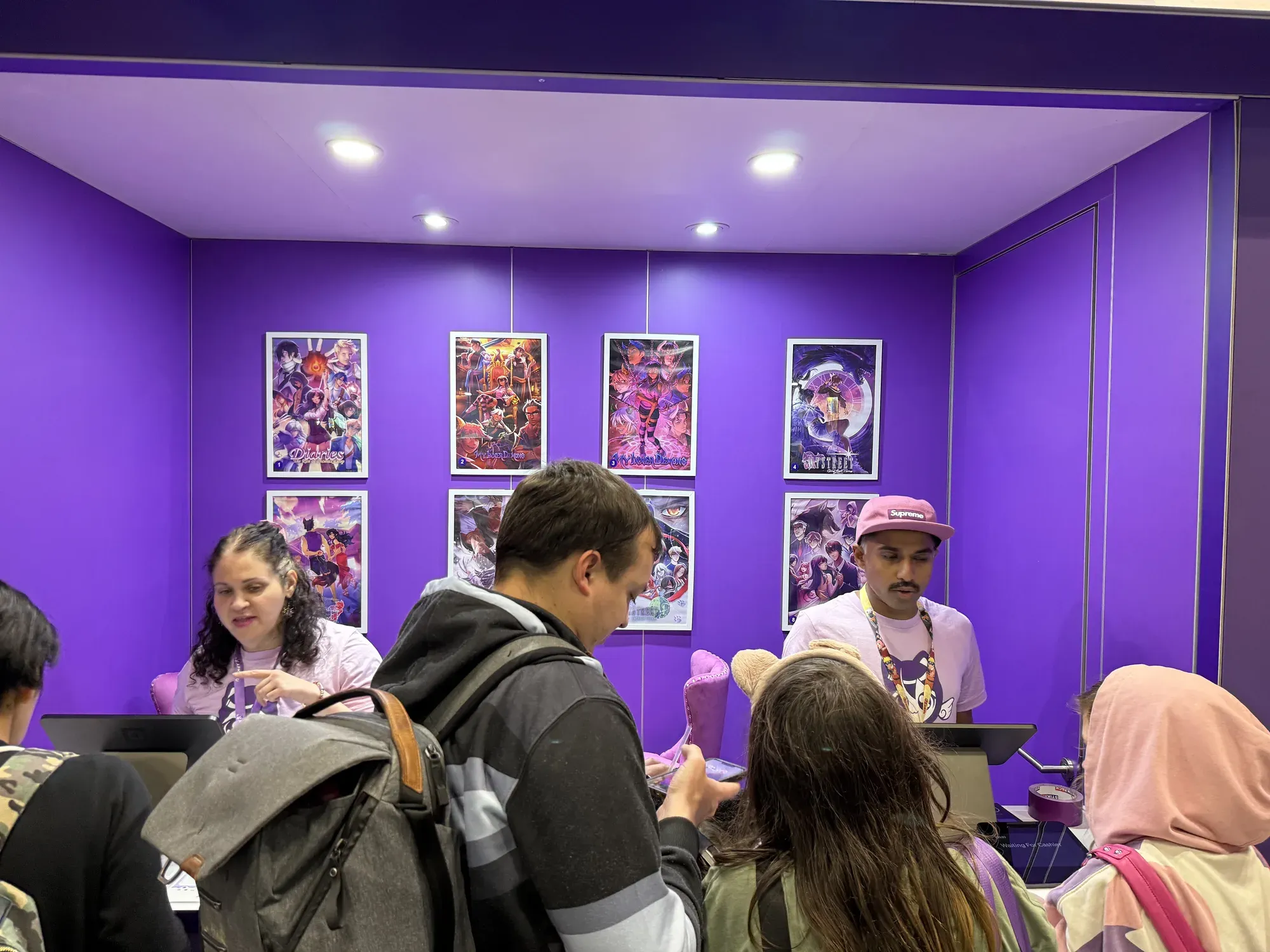 Staff at the Aphmau's Mini Mart counter serving fans in front of a wall of framed Aphmau posters