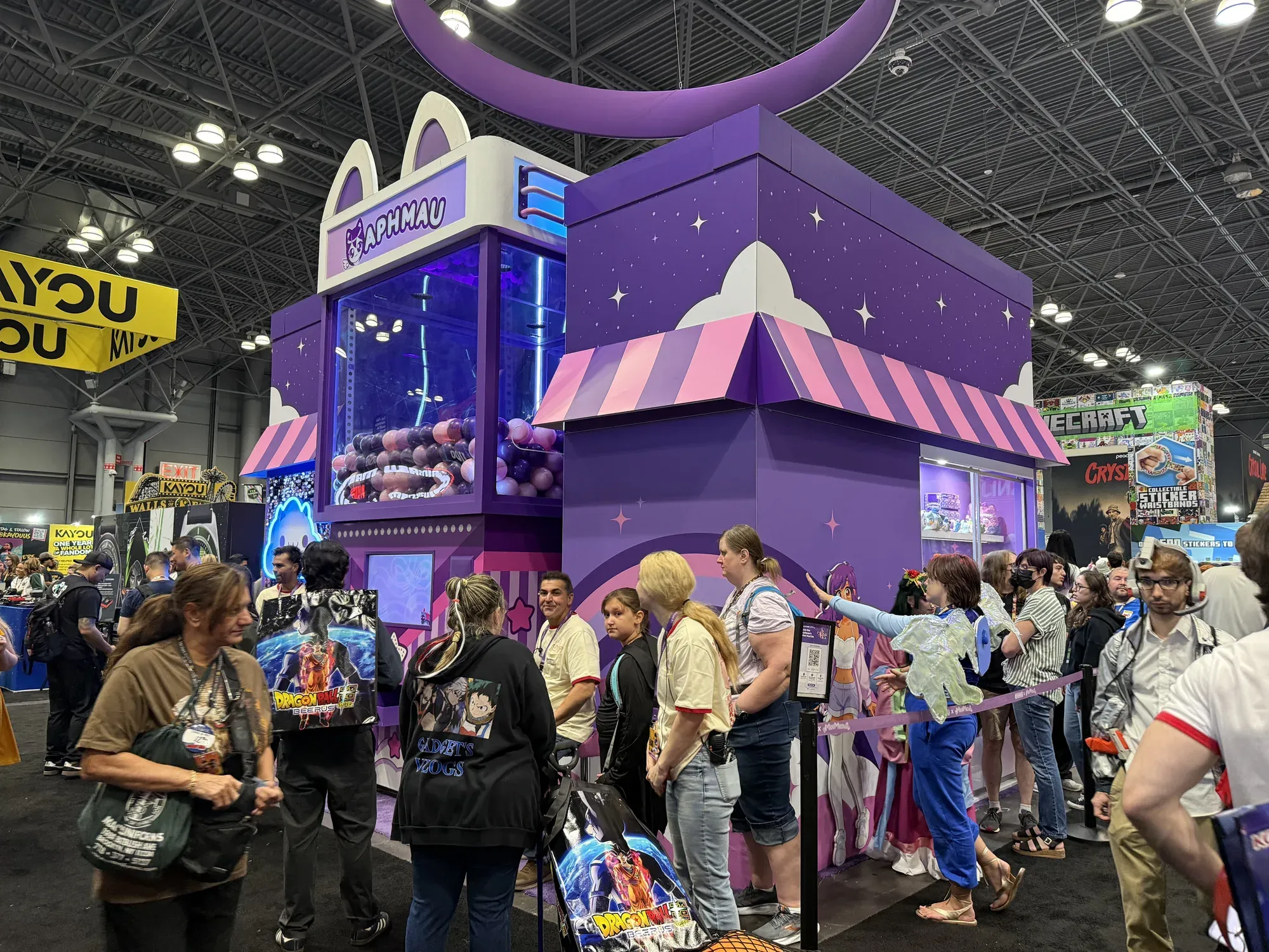 Fans lining up at Aphmau's Mini Mart at New York Comic Con, beside its giant Aphmau gumball machine and a stand with a QR code to join the line