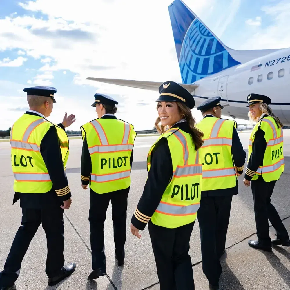 United Airlines pilots in high-visibility vests walking on the tarmac beside a United plane