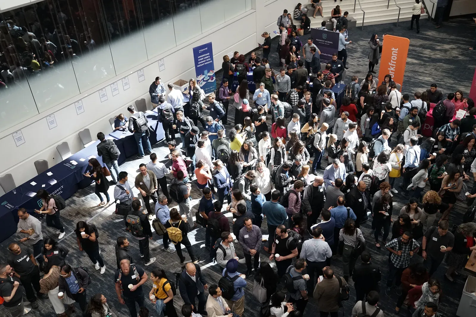 Overhead view of a packed conference hall with crowds of attendees around sponsor tables and banners