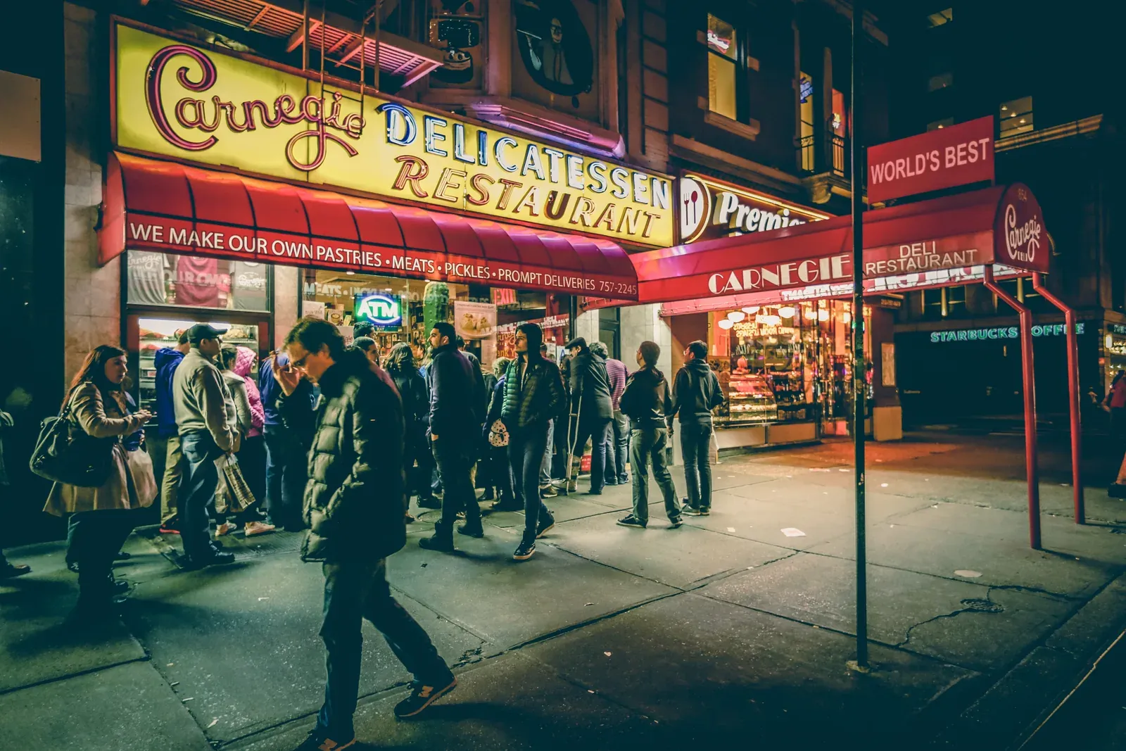 Crowd lined up outside Carnegie Deli in New York at night under its neon signs