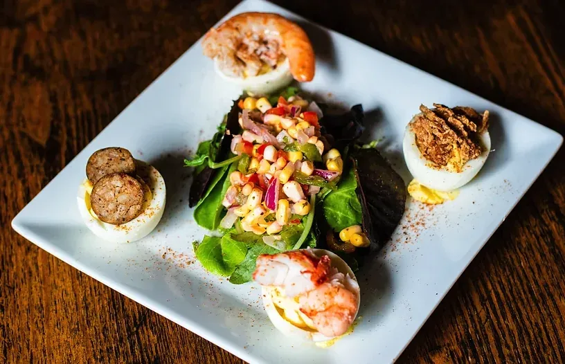 Twisted Soul deviled eggs topped with shrimp, sausage, and crispy onions around a corn salad on greens
