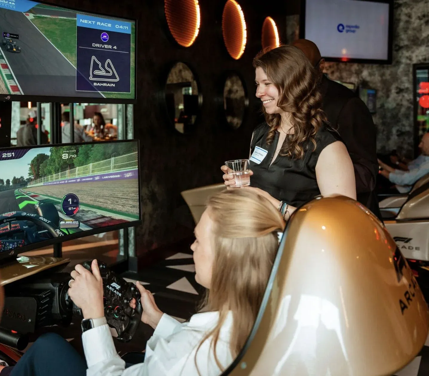 A guest at the wheel of an F1 Arcade racing simulator while others look on