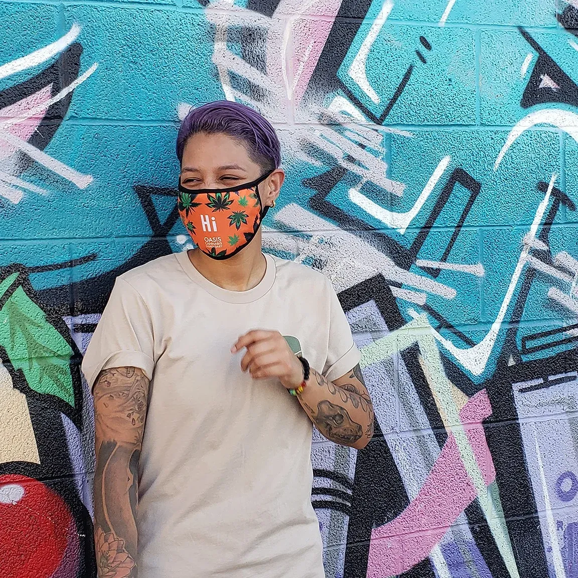 Oasis staff member in a cannabis-leaf face mask in front of a mural