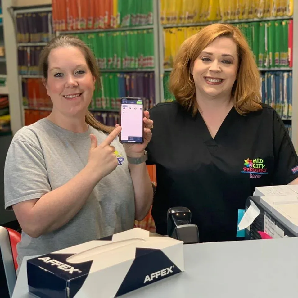 Two Mid City Pediatrics staff members, one holding up a phone