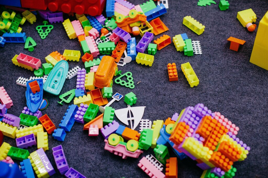 Vibrant plastic toy blocks scattered on a grey carpet, showcasing assorted shapes and colors.