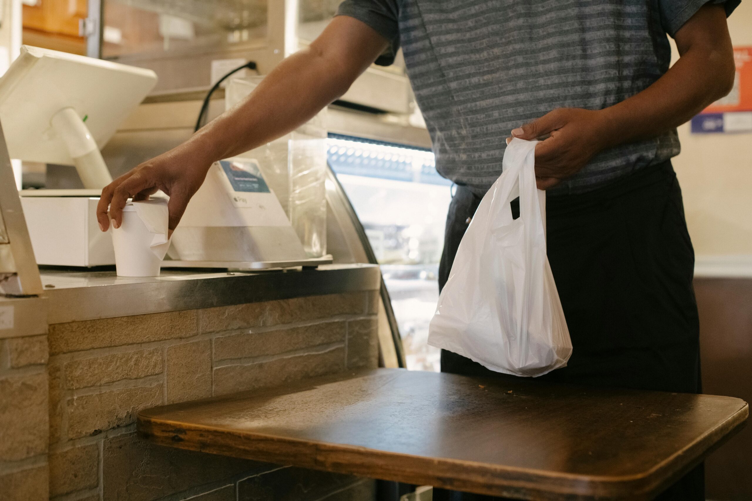 Unrecognizable male picking up takeaway order and cup in a casual cafe setting.