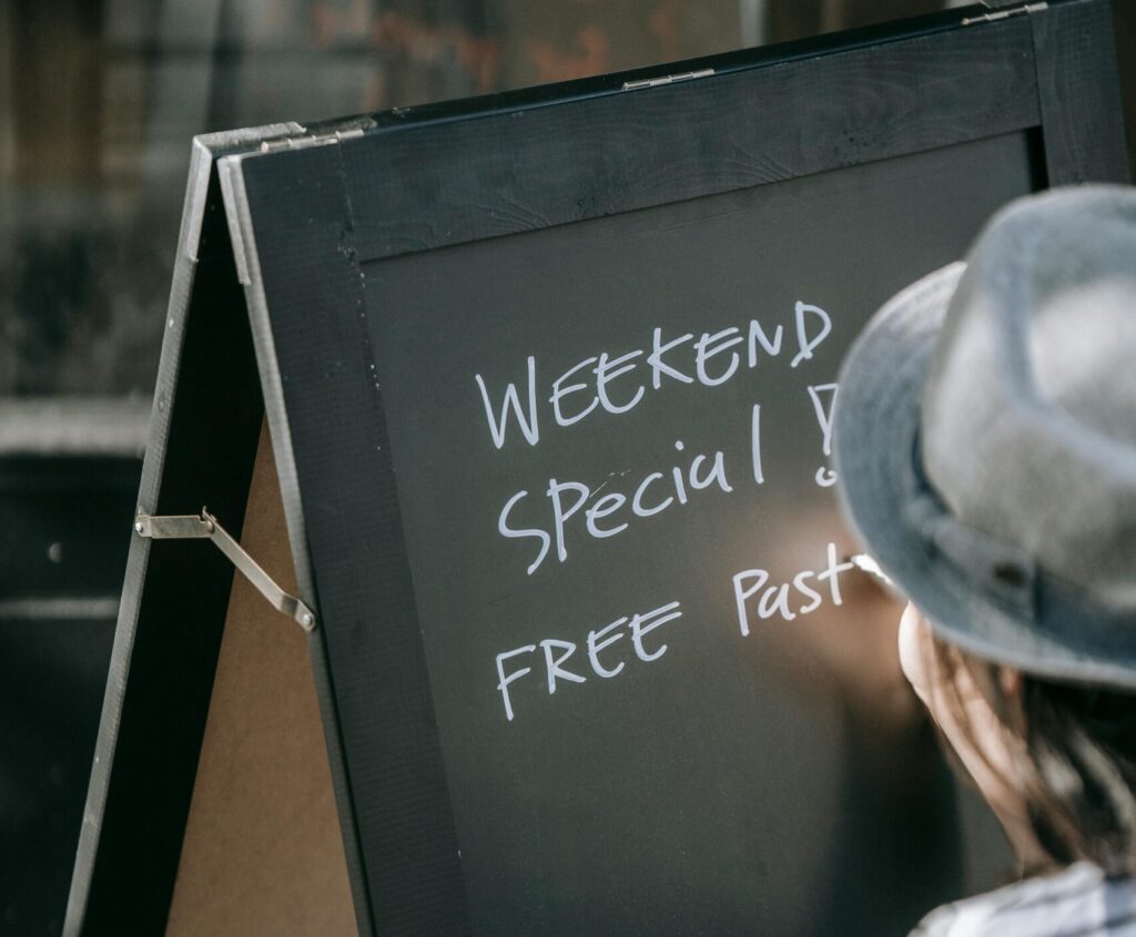 A woman in a hat writing weekend specials on an outdoor menu board.