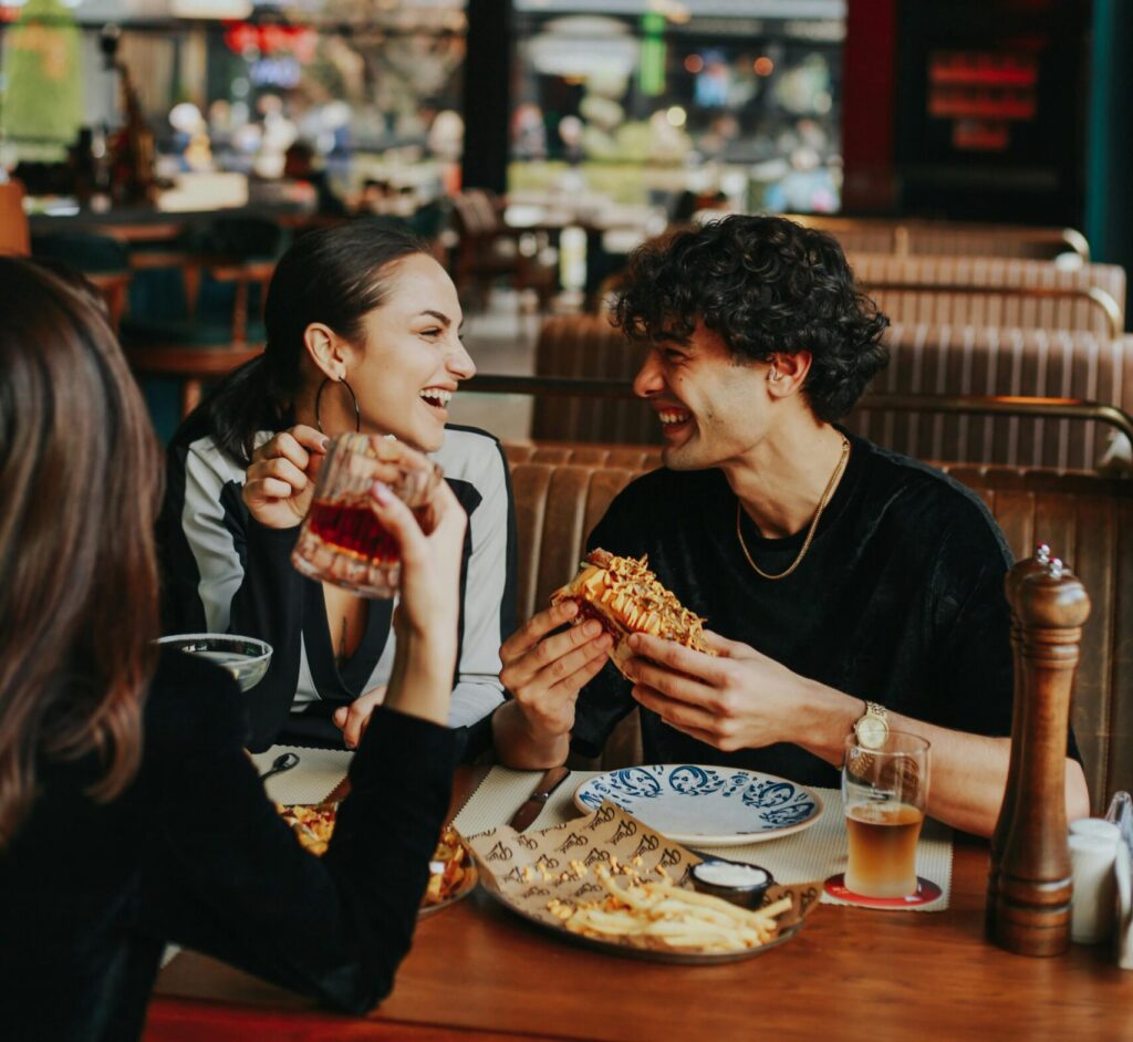 Group of friends sharing food and drinks inside a lively restaurant setting.